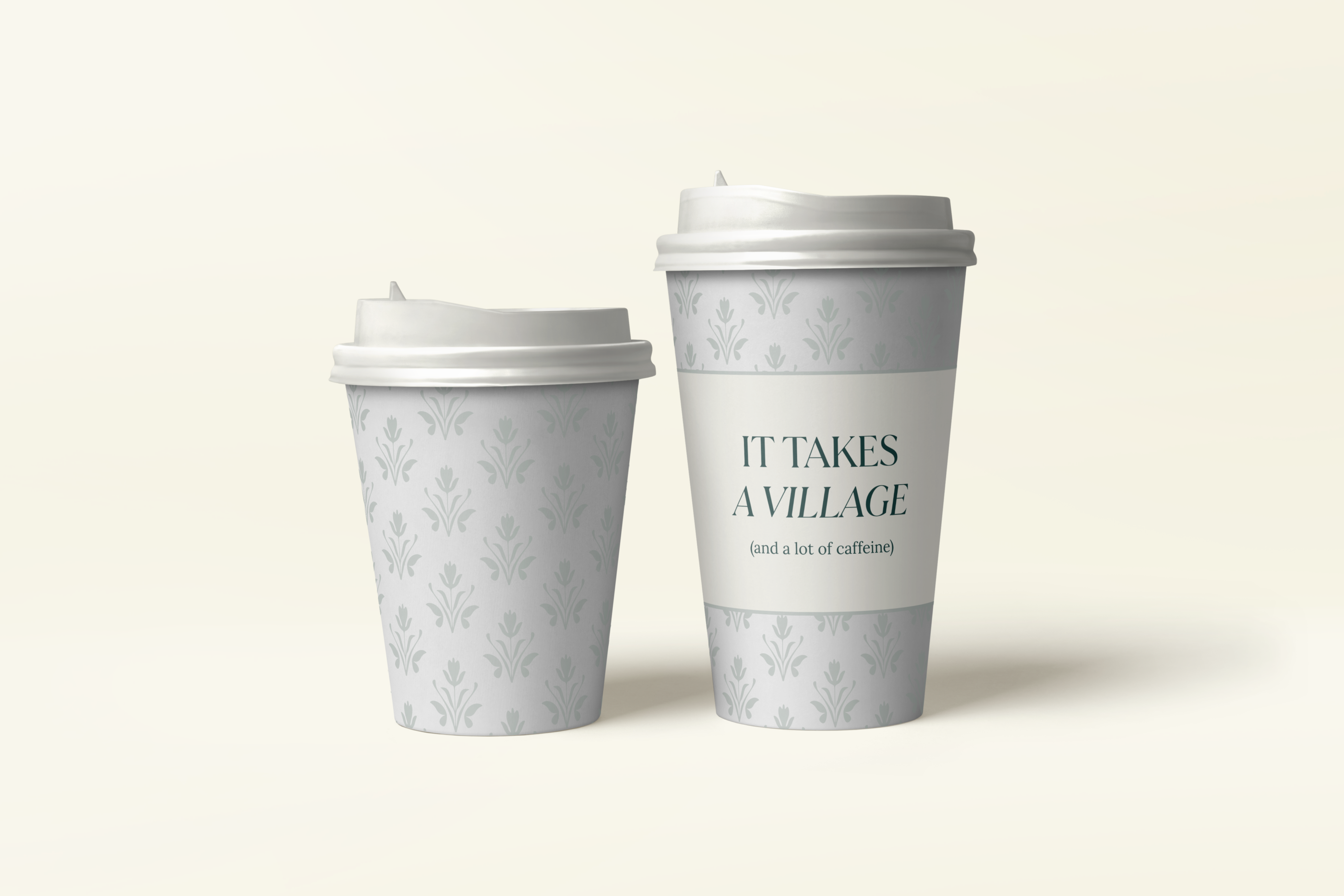 Two coffee cups with damask pattern and white lid, larger cup reads 'It Takes a Village (and a lot of caffeine)