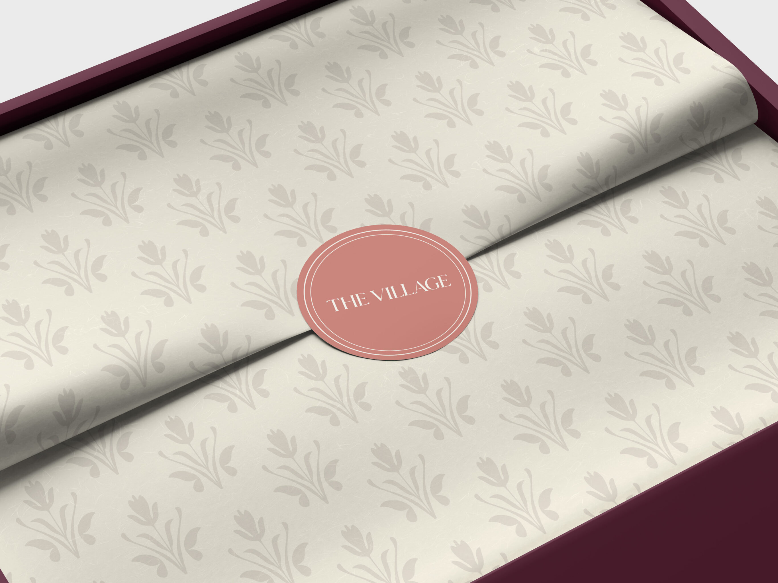 The Village brand identity on cream tissue paper with leaf pattern and burgundy box