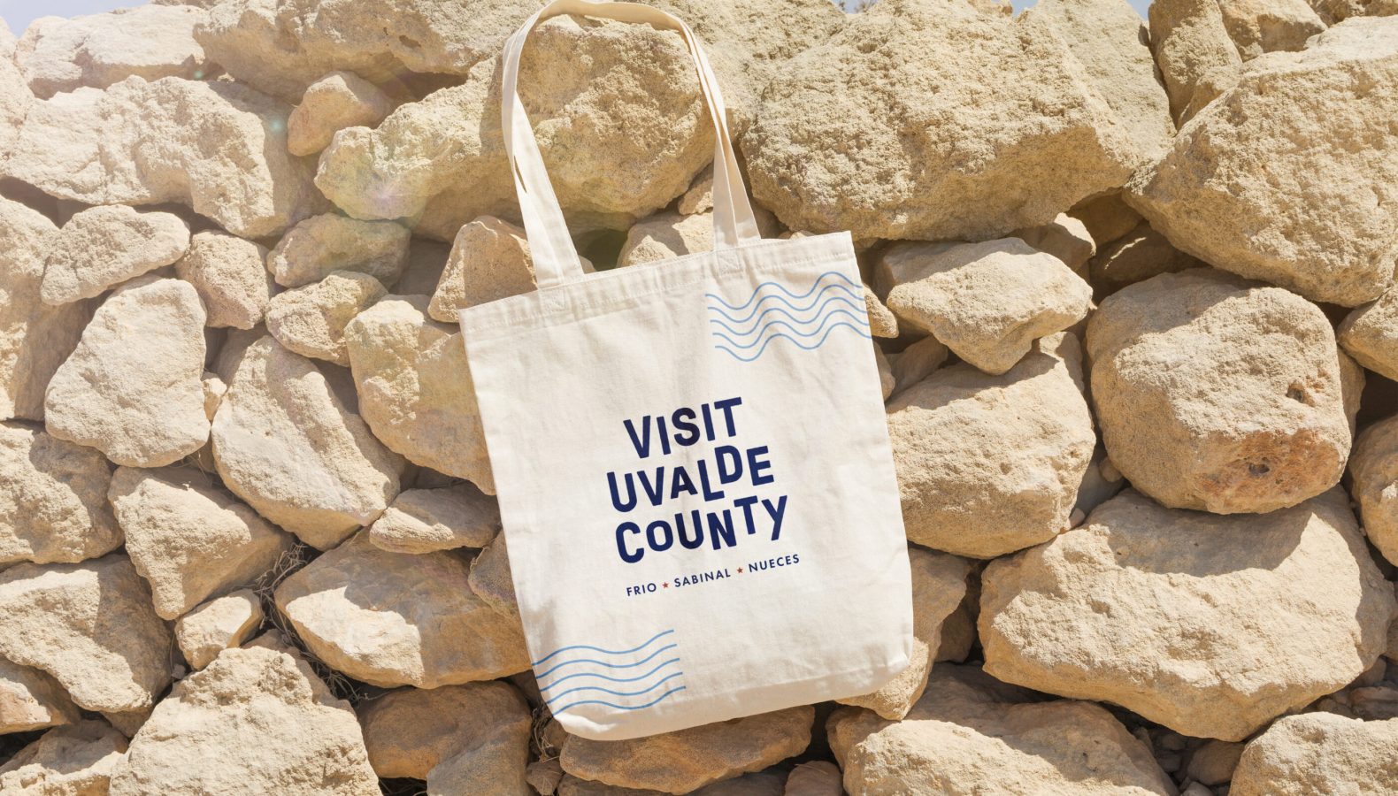 Visit Uvalde County canvas tote bag with blue wave design against tan limestone rocks