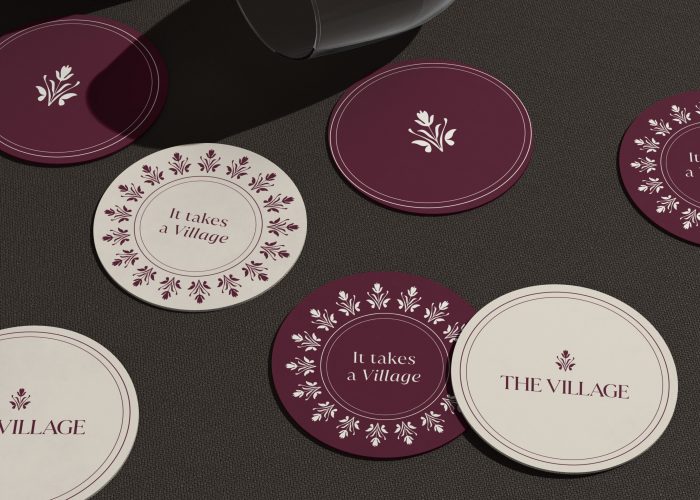 The Village brand coasters in burgundy and cream with floral motifs and tagline