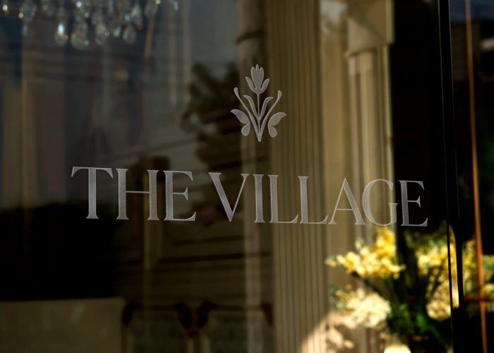 The Village logo etched on glass entrance signage with elegant architectural columns visible behind